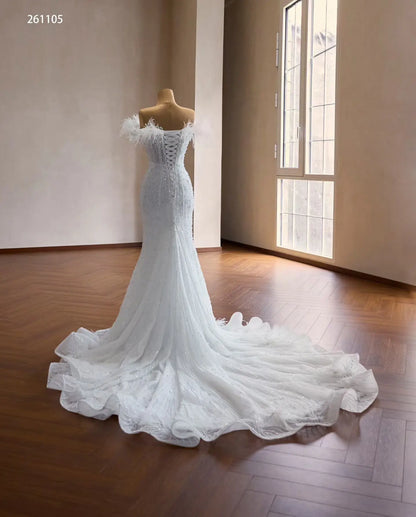 White mermaid wedding dress with feather-trimmed off-shoulder neckline, beaded bodice, corset back, and ruffled flared hem.