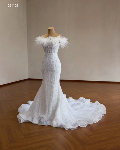 White mermaid wedding dress with feather-trimmed off-shoulder neckline, vertical pearl beading, and ruffled flared hem.