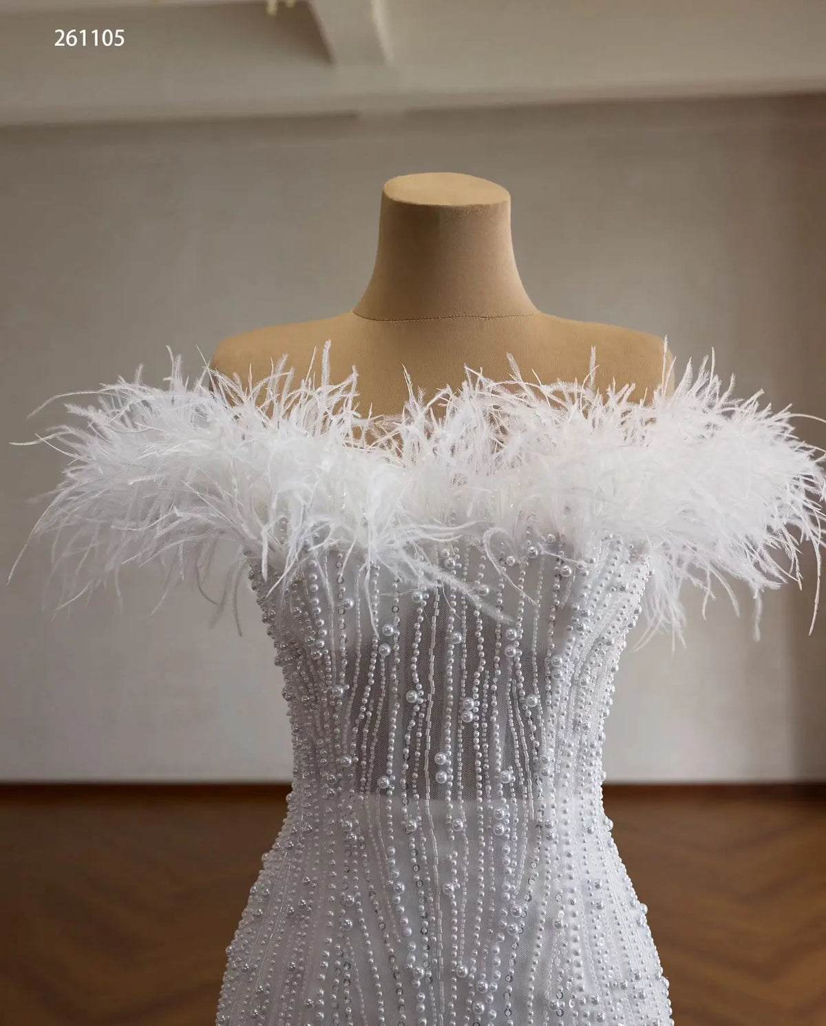 White off-shoulder mermaid wedding dress featuring feather trim, vertical pearl beading, and crystal embellishments.
