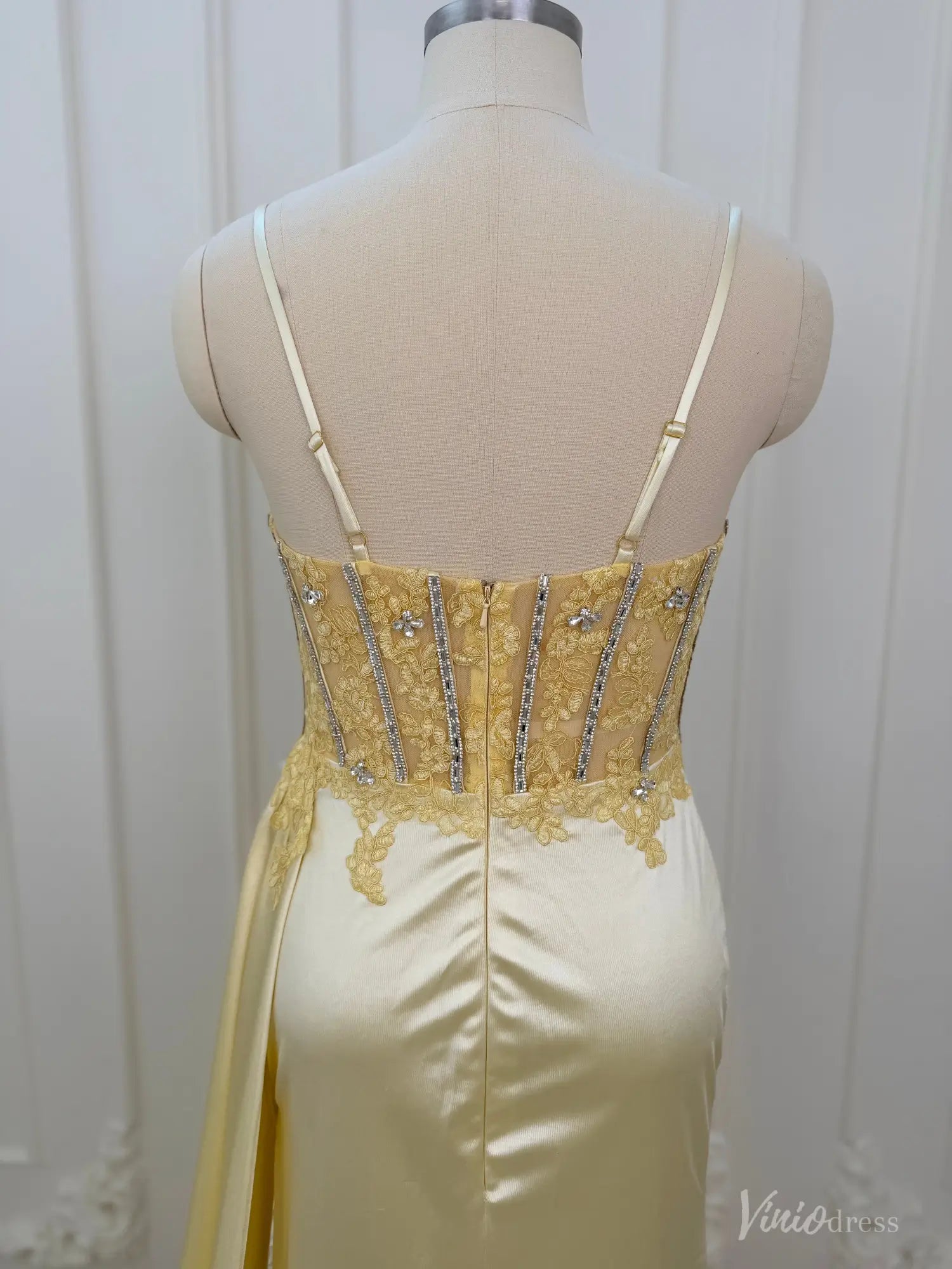 Back view of a yellow satin corset prom dress with a beaded bodice, spaghetti straps, and lace detailing on a mannequin.