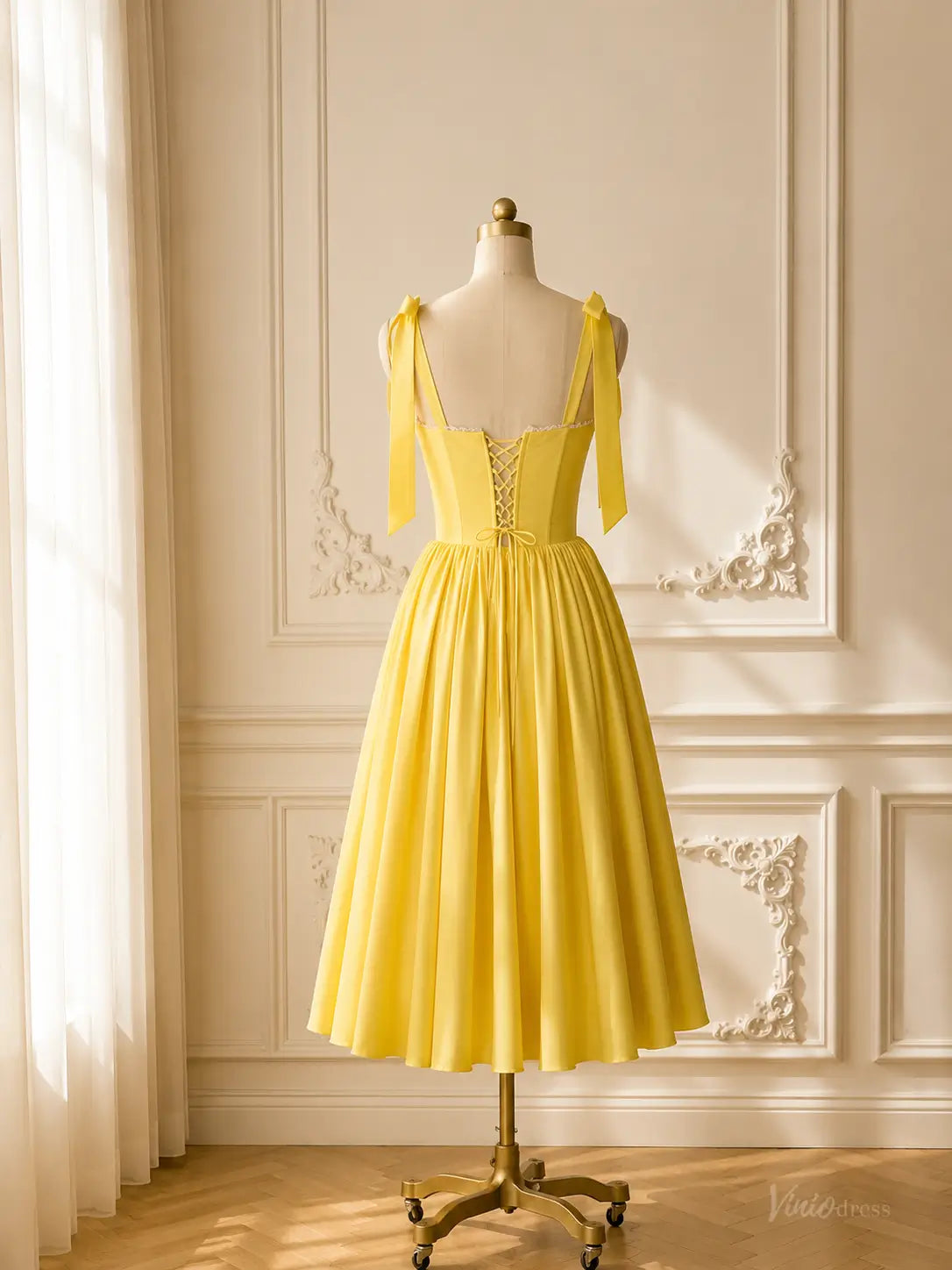 Yellow tea-length prom dress with a corset bodice, bow straps, and lace-up back on a mannequin.